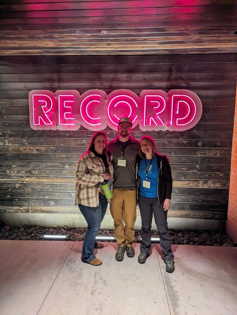 Photo of three people posing in front of the building sign.